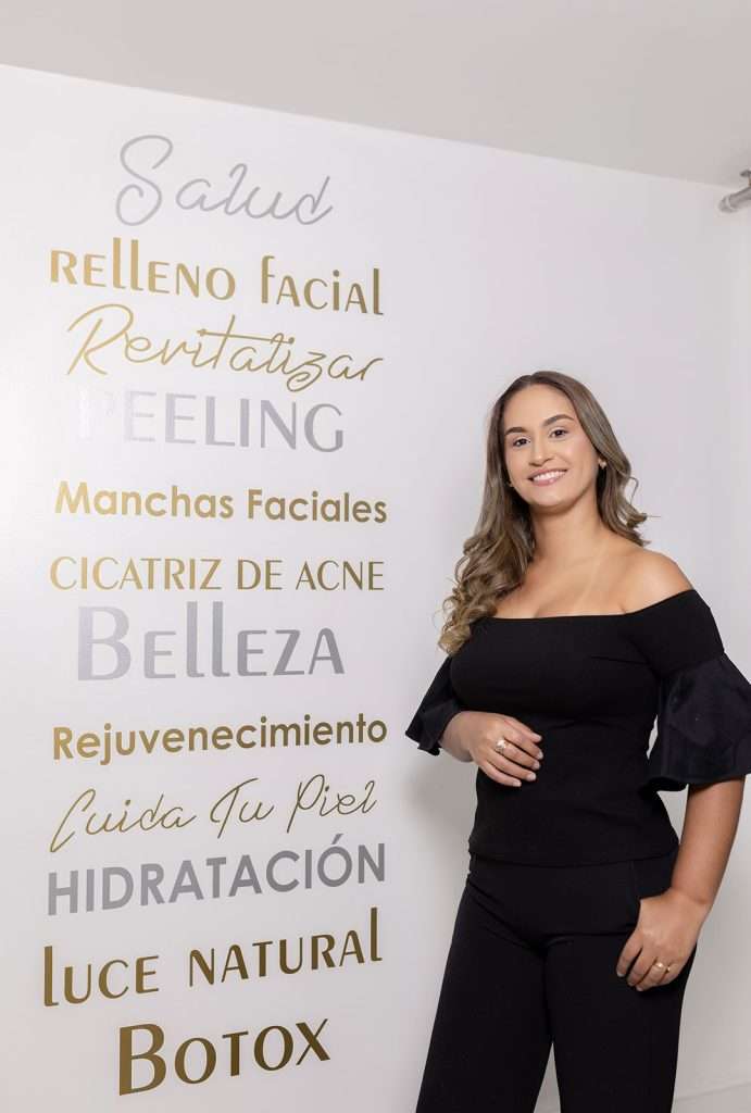 Doctora Karina de pie con blusa y pantalón negro junto a listado de servicios.